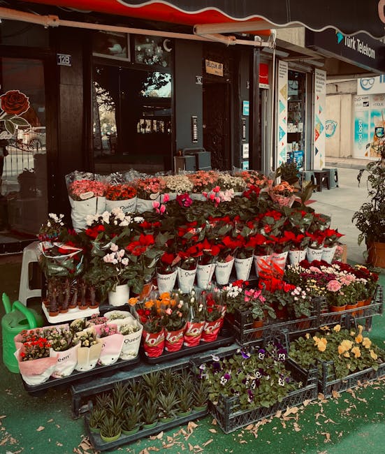 An outdoor flower display in front of Gants Hill florist, showcasing a variety of fresh flowers including red roses, pink tulips, white lilies, and multicoloured mixed bouquets arranged on black plast