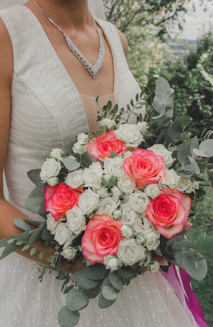 A bride holds a large floral bouquet featuring vibrant pink roses, white spray roses, and lush green eucalyptus leaves. The bouquet is arranged in a round, dense style with flowers tightly grouped tog